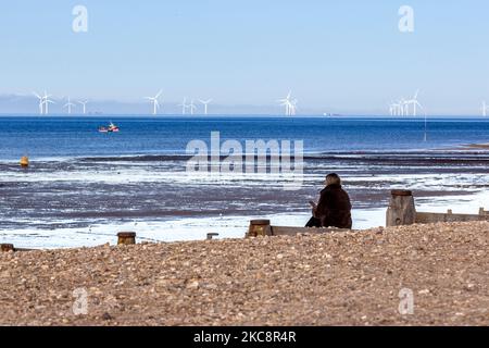 Une femme est vue assis sur une plage en face des moulins à vent assurant une distanciation sociale lors d'une journée froide ensoleillée d'hiver à Whitstable, ville côtière du sud-est de l'Angleterre comme verrouillage strict du coronavirus - la politique de séjour à domicile de niveau 4 - se poursuit au Royaume-Uni en raison du nombre élevé de cas Covid-19 dans le pays - 5 février 2021. Le soleil a conduit les gens hors de leurs maisons, toujours la communauté observe la distanciation sociale. L'exercice, la marche des chiens et l'entrée au travail sont des exceptions dans la politique de séjour à la maison (photo par Dominika Zarzycka/NurPhoto) Banque D'Images