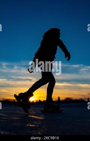 Silhouettes sombres de personnes pendant le patinage sur glace sur le lac naturel gelé cristal dans la région du Brabant Nord dans l'après-midi avant le coucher du soleil. La frénésie du patinage sur glace prend le dessus des pays-Bas. Les Hollandais s'amusent et apprécient le temps enneigé froid d'une semaine avec des températures inférieures à zéro qui font geler les lacs, les ruisseaux, les étangs, les rivières et les canaux. La foule a été le patinage dans le parc Meerland près de la ville d'Eindhoven, pendant un ciel bleu ensoleillé jour, comme c'est une tradition hollandaise, les gens sont également vus à l'extérieur dans la nature glacée et l'environnement froid marchant sur la glace des lacs gelés, p Banque D'Images