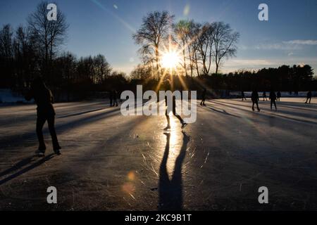 Silhouettes sombres de personnes pendant le patinage sur glace sur le lac naturel gelé cristal dans la région du Brabant Nord dans l'après-midi avant le coucher du soleil. La frénésie du patinage sur glace prend le dessus des pays-Bas. Les Hollandais s'amusent et apprécient le temps enneigé froid d'une semaine avec des températures inférieures à zéro qui font geler les lacs, les ruisseaux, les étangs, les rivières et les canaux. La foule a été le patinage dans le parc Meerland près de la ville d'Eindhoven, pendant un ciel bleu ensoleillé jour, comme c'est une tradition hollandaise, les gens sont également vus à l'extérieur dans la nature glacée et l'environnement froid marchant sur la glace des lacs gelés, p Banque D'Images