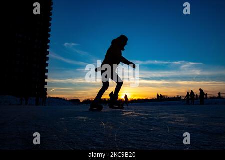 Silhouettes sombres de personnes pendant le patinage sur glace sur le lac naturel gelé cristal dans la région du Brabant Nord dans l'après-midi avant le coucher du soleil. La frénésie du patinage sur glace prend le dessus des pays-Bas. Les Hollandais s'amusent et apprécient le temps enneigé froid d'une semaine avec des températures inférieures à zéro qui font geler les lacs, les ruisseaux, les étangs, les rivières et les canaux. La foule a été le patinage dans le parc Meerland près de la ville d'Eindhoven, pendant un ciel bleu ensoleillé jour, comme c'est une tradition hollandaise, les gens sont également vus à l'extérieur dans la nature glacée et l'environnement froid marchant sur la glace des lacs gelés, p Banque D'Images