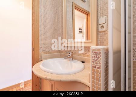 Toilette avec petite commode blanche avec miroir en bois assorti et carrelage beige sur les murs Banque D'Images