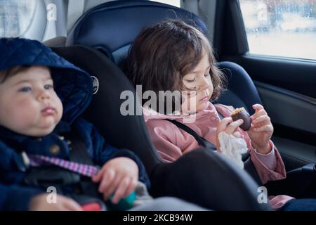 frères et sœurs dans les sièges d'auto ayant des collations dans le siège arrière d'une voiture un jour pluvieux Banque D'Images