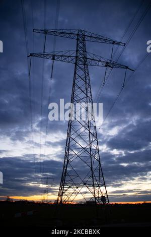 Poteaux électriques haute tension pendant l'heure magique. Les tours métalliques, vues au coucher du soleil dans la campagne hollandaise, distribuent l'énergie électrique de la centrale électrique, de la Belgique et de l'Allemagne à travers le pays. Les fils électriques, la grille et les piliers ou les pylônes de puissance sont vus comme des silhouettes dans le ciel nuageux et coloré de crépuscule. Stevensweert, pays-Bas sur 19 mars 2021 (photo de Nicolas Economou/NurPhoto) Banque D'Images