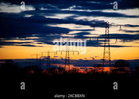 Poteaux électriques haute tension pendant l'heure magique. Les tours métalliques, vues au coucher du soleil dans la campagne hollandaise, distribuent l'énergie électrique de la centrale électrique, de la Belgique et de l'Allemagne à travers le pays. Les fils électriques, la grille et les piliers ou les pylônes de puissance sont vus comme des silhouettes dans le ciel nuageux et coloré de crépuscule. Stevensweert, pays-Bas sur 19 mars 2021 (photo de Nicolas Economou/NurPhoto) Banque D'Images