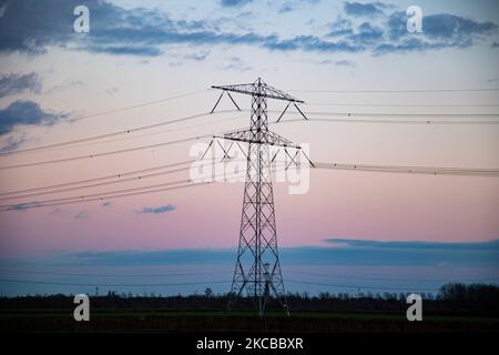 Poteaux électriques haute tension pendant l'heure magique. Les tours métalliques, vues au coucher du soleil dans la campagne hollandaise, distribuent l'énergie électrique de la centrale électrique, de la Belgique et de l'Allemagne à travers le pays. Les fils électriques, la grille et les piliers ou les pylônes de puissance sont vus comme des silhouettes dans le ciel nuageux et coloré de crépuscule. Stevensweert, pays-Bas sur 19 mars 2021 (photo de Nicolas Economou/NurPhoto) Banque D'Images