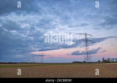 Poteaux électriques haute tension pendant l'heure magique. Les tours métalliques, vues au coucher du soleil dans la campagne hollandaise, distribuent l'énergie électrique de la centrale électrique, de la Belgique et de l'Allemagne à travers le pays. Les fils électriques, la grille et les piliers ou les pylônes de puissance sont vus comme des silhouettes dans le ciel nuageux et coloré de crépuscule. Stevensweert, pays-Bas sur 19 mars 2021 (photo de Nicolas Economou/NurPhoto) Banque D'Images