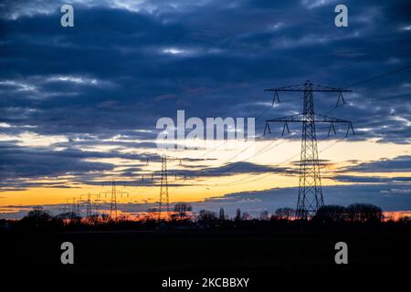 Poteaux électriques haute tension pendant l'heure magique. Les tours métalliques, vues au coucher du soleil dans la campagne hollandaise, distribuent l'énergie électrique de la centrale électrique, de la Belgique et de l'Allemagne à travers le pays. Les fils électriques, la grille et les piliers ou les pylônes de puissance sont vus comme des silhouettes dans le ciel nuageux et coloré de crépuscule. Stevensweert, pays-Bas sur 19 mars 2021 (photo de Nicolas Economou/NurPhoto) Banque D'Images