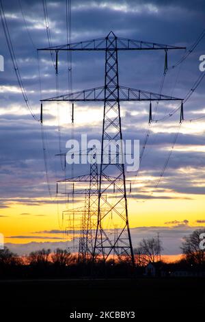 Poteaux électriques haute tension pendant l'heure magique. Les tours métalliques, vues au coucher du soleil dans la campagne hollandaise, distribuent l'énergie électrique de la centrale électrique, de la Belgique et de l'Allemagne à travers le pays. Les fils électriques, la grille et les piliers ou les pylônes de puissance sont vus comme des silhouettes dans le ciel nuageux et coloré de crépuscule. Stevensweert, pays-Bas sur 19 mars 2021 (photo de Nicolas Economou/NurPhoto) Banque D'Images