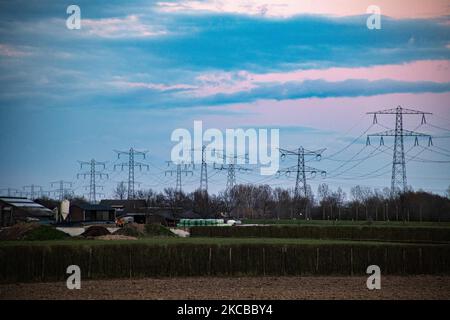 Poteaux électriques haute tension pendant l'heure magique. Les tours métalliques, vues au coucher du soleil dans la campagne hollandaise, distribuent l'énergie électrique de la centrale électrique, de la Belgique et de l'Allemagne à travers le pays. Les fils électriques, la grille et les piliers ou les pylônes de puissance sont vus comme des silhouettes dans le ciel nuageux et coloré de crépuscule. Stevensweert, pays-Bas sur 19 mars 2021 (photo de Nicolas Economou/NurPhoto) Banque D'Images