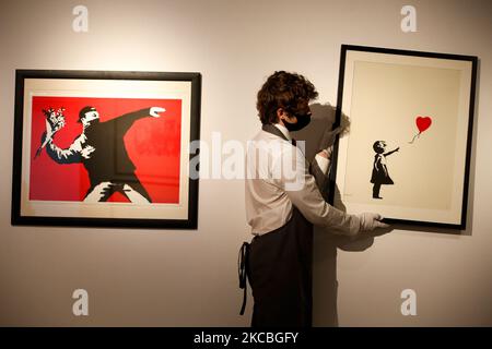 Un maître-maître pose un travail de main de l'artiste britannique Banksy 'Girl with Balloon', et à côté de Banksy 'Love is in the Air', chacun estimé à GBP300 000-500 000, lors d'un aperçu de presse à la maison de vente aux enchères de Christie à Londres, en Angleterre, sur 26 mars 2021. (Photo de David Cliff/NurPhoto) Banque D'Images