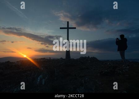 Un homme prend une photo de la Croix de l'année Sainte au sommet de Bray Head au coucher du soleil, pendant le confinement de la COVID-19. Le jeudi 15 avril 2021, à Bray, comté de Wicklow, Irlande. (Photo par Artur Widak/NurPhoto) Banque D'Images