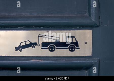 Vue rapprochée partielle de la barrière verte texturée avec panneau en laiton métallique monté sur celle-ci avec un camion de remorquage remorquant une voiture comme avis d'absence de stationnement et les zones à k Banque D'Images