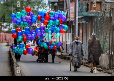 Les hommes de Kashmiri portant un masque se promène devant un vendeur de ballons lors du festival musulman d'Eid-UL-Fitr dans le cadre de la pandémie du coronavirus COVID-19 à Sopore, district de Baramulla, Jammu-et-Cachemire, Inde, le 13 mai 2021. Les célébrations de l'EID-ul-Fitr au Cachemire ont été une affaire peu importante jeudi, alors que les fidèles ont marqué l'aboutissement du mois de jeûne de Ramzan en offrant les prières d'action de grâce dans les petites congrégations locales en observant les distances sociales en vue de la pandémie de COVID-19. Aucune prière d'Eid n'a été offerte pour la quatrième fois consécutive dans les mosquées et les sanctuaires majeurs du Cachemire comme étant polique Banque D'Images