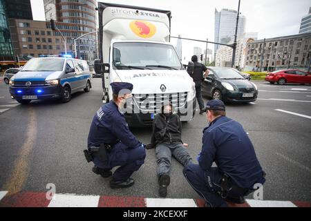 La police parle à Weronika (20) qui participe à une action spontanée pour bloquer une fourgonnette à Varsovie, en Pologne, sur 19 mai 2021. Des militants anti-avortement dans une fourgonnette affichant des images graphiques de fœtus avortés ont été arrêtés par des activistes pro-choix dans le centre de Varsovie, en Pologne. Weronika, activiste pro-choix âgé de vingt ans, s'est assis sur la route en face du bus, car il s'agissait de la sortie du rond-point animé de l'ONZ. Les chauffeurs du bus ont fait retentir une alarme forte par les haut-parleurs de la camionnette pour tenter de repousser l’activiste. Deux autres femmes, Magda et lu se sont accroupissé sous le bus. Plusieurs dizaines de policiers sont arrivés bientôt Banque D'Images