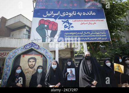 Les femmes voilées portant un masque facial protecteur portent le drapeau du Hezbollah libanais et un portrait de l'ancien corps des Gardiens de la révolution islamique (IRGC), le général Qasem Soleimani, Qui a été tué lors d'une attaque par drone américain à l'aéroport de Bagdad, alors qu'il se trouvait sous un panneau d'affichage anti-Israël lors d'un rassemblement sur la place palestinienne dans le centre de Téhéran, sur 22 mai 2021. Un groupe d'hommes et de femmes iraniens se sont réunis sur la place palestinienne pour célébrer la victoire des Palestiniens sur Israël, selon la déclaration lue par un manifestant. (Photo de Morteza Nikoubazl/NURP Banque D'Images