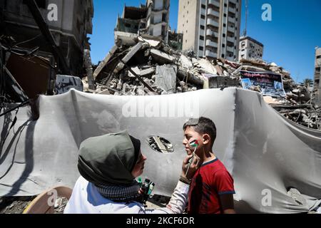 L'artiste palestinien Etaf al-Najili, 28 ans, peint le drapeau palestinien sur les visages des enfants près du site des frappes aériennes israéliennes dans la ville de Gaza, sur 24 mai 2021. (Photo de Majdi Fathi/NurPhoto) Banque D'Images