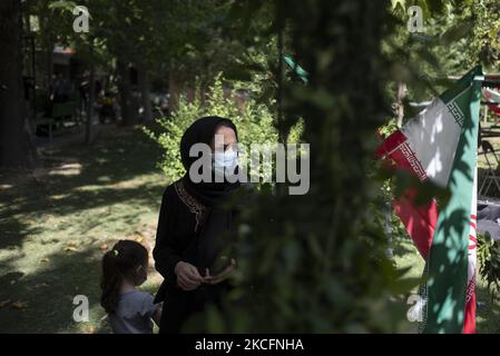 Une iranienne portant un masque facial protecteur regarde pendant qu’elle se tient à côté d’un drapeau iranien alors qu’elle assiste aux funérailles de deux martyrs adolescents non identifiés dans un parc local du centre-ville de Téhéran, sur 6 juin 2021 (1980-88). (Photo de Morteza Nikoubazl/NurPhoto) Banque D'Images