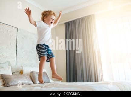 Le lit est mon trampoline. Un adorable petit garçon sautant sur le lit à la maison. Banque D'Images