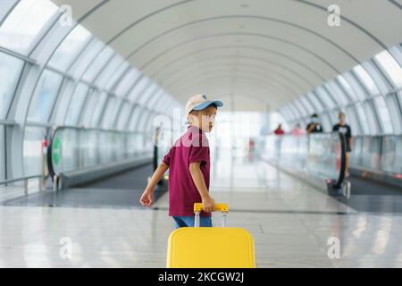 Un garçon asiatique avec une valise jaune T-shirt et un short marchant dans le terminal de l'aéroport se prépare à embarquer à la porte pour un vol en avion. Banque D'Images