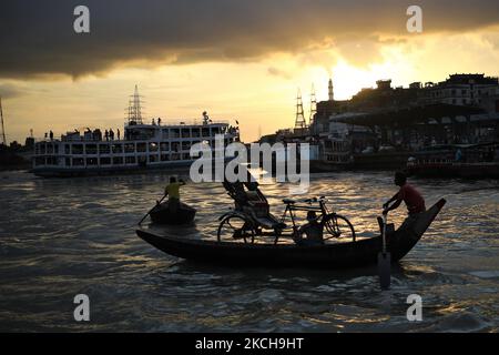 Un arrache-pousse tient son pousse-pousse alors qu'il traverse le fleuve Buriganga en bateau à l'aube à Dhaka, au Bangladesh, sur 15 juillet 2021. (Photo de Syed Mahamudur Rahman/NurPhoto) Banque D'Images