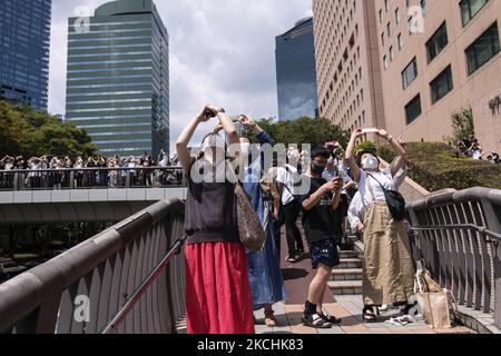 Les gens pointent leurs mobiles vers le ciel pour prendre une photo de l'escadron de libre-défense aérienne Blue Impulse dessinant les anneaux olympiques au-dessus de Tokyo, Japon, le 23 juillet 2021. (Photo par Yusuke Harada/NurPhoto) Banque D'Images