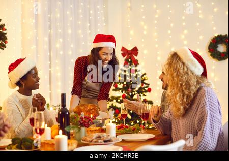 Bonne jeune femme servant un repas festif à des amis à la table du dîner de Noël à la maison Banque D'Images