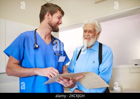 Votre dossier montre de grands progrès. Un jeune médecin et son patient âgé discutent de ses dossiers médicaux ensemble. Banque D'Images