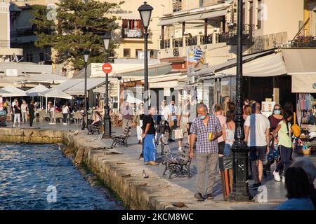 Les habitants et les touristes sont vus avec facemask à pied à la promenade du front de mer de l'ancien port vénitien de la ville de Chania avec les petites boutiques, tavernes, cafés et restaurants autour ainsi que le célèbre phare, la mosquée, les chantiers navals vénitiens et les monuments anciens et les monuments près du port et de la mer Égée. La Grèce tente de stimuler son tourisme et de donner des privilèges pour se faire vacciner contre la pandémie du coronavirus Covid-19, les touristes internationaux et les habitants, car le pays est fortement tributaire de l'industrie du tourisme et des voyages malgré le nombre inquiétant de cas avec le Coro Covid-19 Banque D'Images