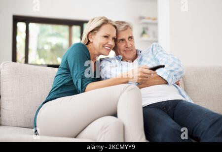 Voyons ce qui se trouve sur la télé. Un couple affectueux et mature regardant la télévision ensemble à la maison. Banque D'Images