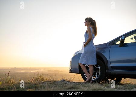 Une jeune femme pilote se reposant près de sa voiture pour profiter d'une chaude soirée d'été. Concept de voyage et d'escapade Banque D'Images