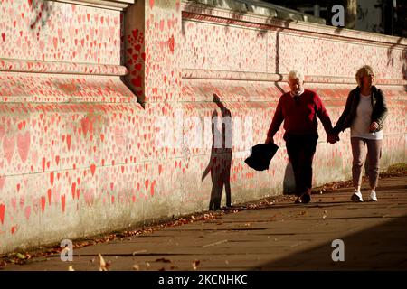 Une promenade en couple à côté du mur commémoratif national des Covid, sur le sentier de la rive sud de la Tamise, en face du Parlement à Londres, en Angleterre, sur 27 septembre 2021. Le mur, créé ce printemps, se compose de plus de 150 000 coeurs peints, chacun représentant une vie perdue dans le pays à Covid-19. (Photo de David Cliff/NurPhoto) Banque D'Images