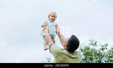 été, dans le jardin, la mère, une vue d'en dessous, le papa jette sa fille d'un an, joue avec elle, a du plaisir. Elle rit et la famille passe son temps libre ensemble. Photo de haute qualité Banque D'Images