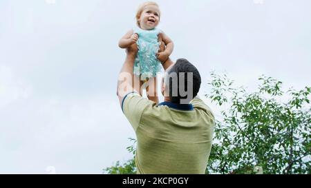 été, dans le jardin, la mère, une vue d'en dessous, le papa jette sa fille d'un an, joue avec elle, a du plaisir. Elle rit et la famille passe son temps libre ensemble. Photo de haute qualité Banque D'Images