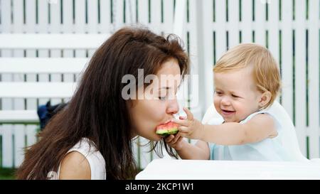 été, dans le jardin, une drôle de fille blonde d'un an traite sa mère avec de la pastèque, la nourrit de ses mains, la fille mange également de la pastèque. Photo de haute qualité Banque D'Images