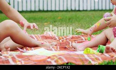 les petits enfants, un garçon de quatre ans et une fille, un frère et une sœur d'un an, jouent ensemble, peignent avec des peintures au doigt, dans le jardin, assis sur une couverture, sur l'herbe, la pelouse, en été. Photo de haute qualité Banque D'Images
