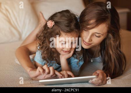 Passer du temps ensemble à la manière numérique. Une mère et une fille heureux de s'amuser à la maison tout en jouant sur une tablette. Banque D'Images