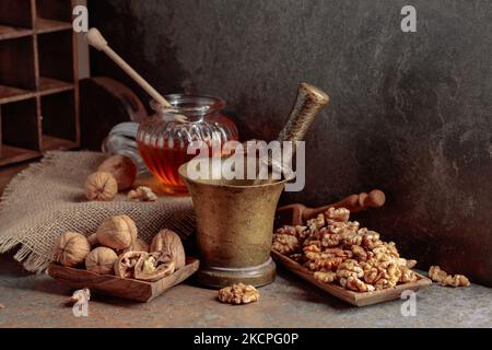 Noix, vieux mortier de laiton et miel sur une table de cuisine. Banque D'Images