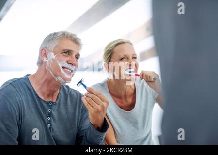 Ils passent leur routine matinale ensemble. Un homme mûr se rasant le visage tandis que sa femme brosse ses dents dans la salle de bains. Banque D'Images