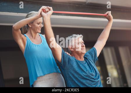 Gardez votre foyer et la douleur Va-t'en. un homme mûr étirant ses muscles de bras avec une bande élastique tout en étant aidé par une femme. Banque D'Images