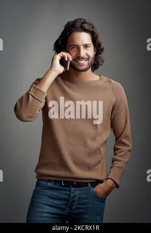 Appelle-moi. ID amour d'entendre de vous. Studio photo d'un beau jeune homme à l'aide d'un téléphone portable pour passer un appel sur fond gris. Banque D'Images