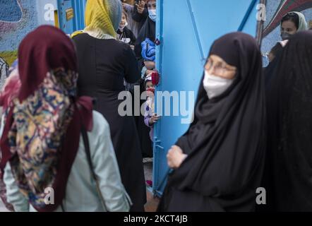 Une écolière afghane portant un masque facial protecteur regarde comme des mères afghanes de jeunes filles et de garçons scolarisés réfugiés attendent leurs enfants tout en se tenant à la porte de l'école Farhang le premier jour de la nouvelle année scolaire? Dans le sud de Téhéran sur 1 novembre 2021. L'école de Farhang a fondé en 2000 par le réfugié afghan Nader Mousavi qui a obtenu une maîtrise en sociologie de l'Université de Téhéran, pour les enfants réfugiés afghans, Et maintenant deux ans après le début de l'épidémie de COVID-19 en Iran, où l'école fonctionnait à temps partiel, elle a commencé à fonctionner à temps plein et Banque D'Images