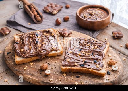 Planche de pain avec pâte de chocolat et bonbons de fête saupoudrer et noisettes sur fond de bois. Nourriture populaire de dessicer. Vue de dessus. Banque D'Images