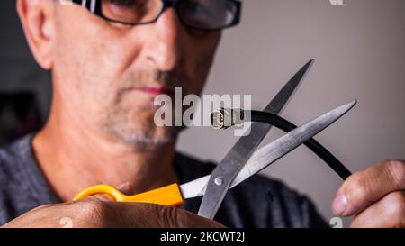 L'homme coupe le câble de télévision avec des ciseaux Banque D'Images