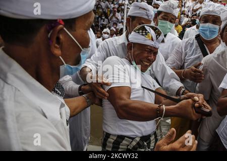 L'homme hindou balinais tente de se poignarder avec le traditionnel dagger de Keris pendant qu'il est en transe pendant le rituel sacré de Ngerebong, au milieu de la pandémie COVID-19 dans le village de Kesiman, Denpasar, Bali, Indonésie sur 28 novembre 2021. Pour la première fois pendant la pandémie, le rituel tenu en cortège complète puisqu'on croit qu'il fait des malheurs et apporte des bénis dans le village ainsi que dans l'univers. (Photo de Johannes Christo/NurPhoto) Banque D'Images