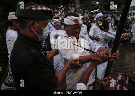 L'homme hindou balinais tente de se poignarder avec le traditionnel dagger de Keris pendant qu'il est en transe pendant le rituel sacré de Ngerebong, au milieu de la pandémie COVID-19 dans le village de Kesiman, Denpasar, Bali, Indonésie sur 28 novembre 2021. Pour la première fois pendant la pandémie, le rituel tenu en cortège complète puisqu'on croit qu'il fait des malheurs et apporte des bénis dans le village ainsi que dans l'univers. (Photo de Johannes Christo/NurPhoto) Banque D'Images