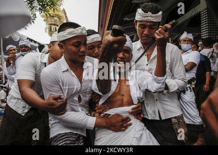 L'homme hindou balinais tente de se poignarder avec le traditionnel dagger de Keris pendant qu'il est en transe pendant le rituel sacré de Ngerebong, au milieu de la pandémie COVID-19 dans le village de Kesiman, Denpasar, Bali, Indonésie sur 28 novembre 2021. Pour la première fois pendant la pandémie, le rituel tenu en cortège complète puisqu'on croit qu'il fait des malheurs et apporte des bénis dans le village ainsi que dans l'univers. (Photo de Johannes Christo/NurPhoto) Banque D'Images