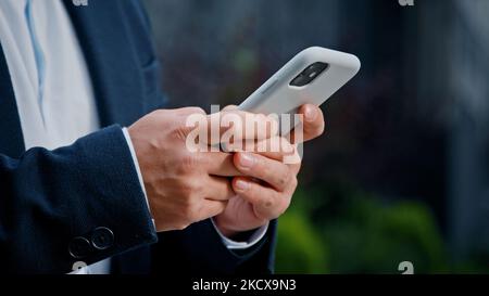 Gros plan mains de sexe masculin saisie de texte navigation sur téléphone mobile. Homme d'affaires inconnu méconnu en costume formel travaillant avec un smartphone en ville Banque D'Images