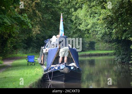 Un homme se tient sur l'arc de son bateau à narrowboat, apparemment en train du réparer pendant qu'il est amarré un après-midi d'été. Banque D'Images