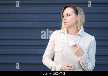 Belle femme blonde d'âge moyen, qui a l'air réfléchie sur le côté devant un mur bleu Banque D'Images
