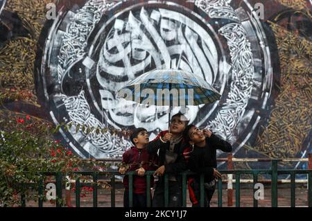 Les enfants palestiniens tiennent un parapluie devant une peinture murale représentant la calligraphie arabe, lors d'une journée de pluie dans la ville de Gaza, sur 17 décembre 2021. - La calligraphie arabe a été inscrite en 2021 sur la liste représentative du patrimoine culturel immatériel de l'humanité par l'Organisation des Nations Unies pour l'éducation, la science et la culture (UNESCO). (Photo de Majdi Fathi/NurPhoto) Banque D'Images